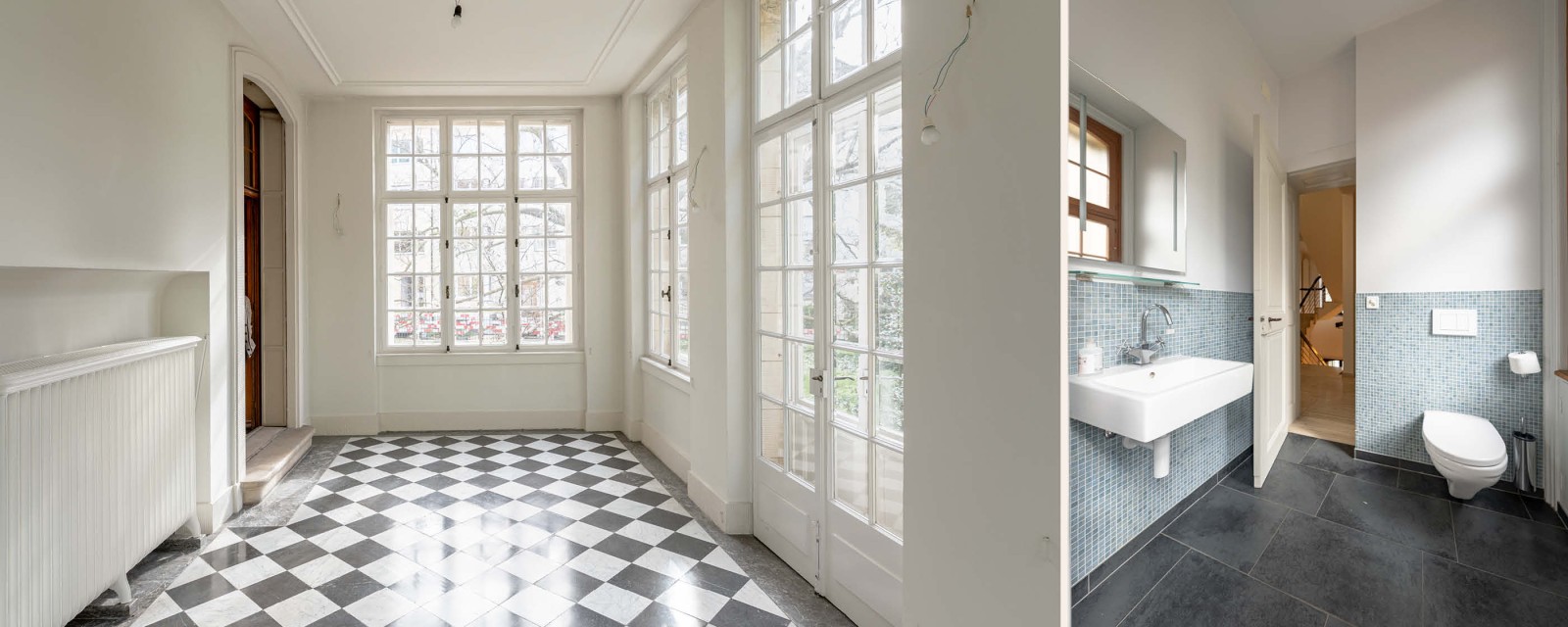 Links ein Raum mit Plattenboden im Schachbrettmuster und rechts ein kleines Badezimmer.